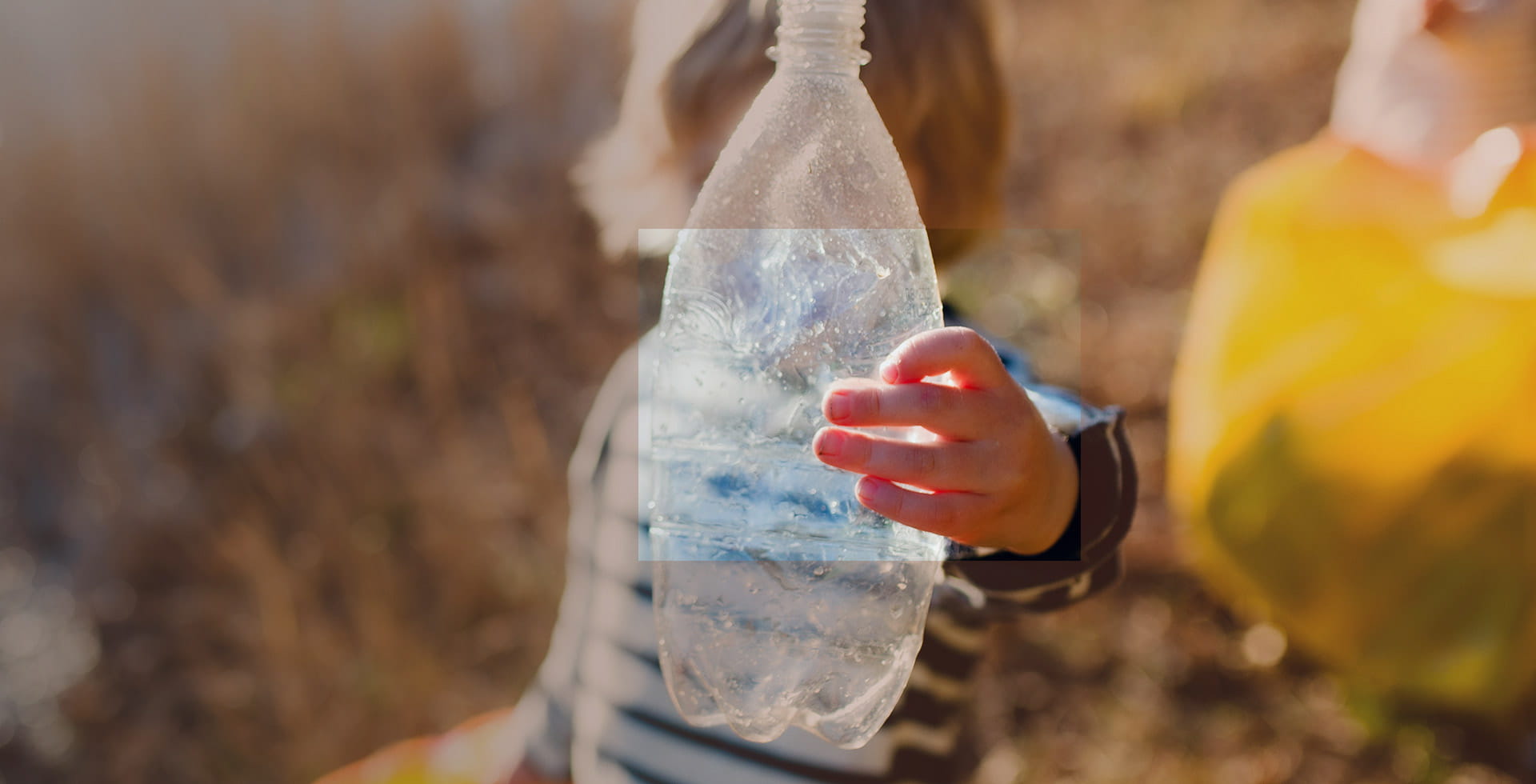 Child holding a plastic bottle against the sunlight - Unwrapping the potential of sustainable packaging