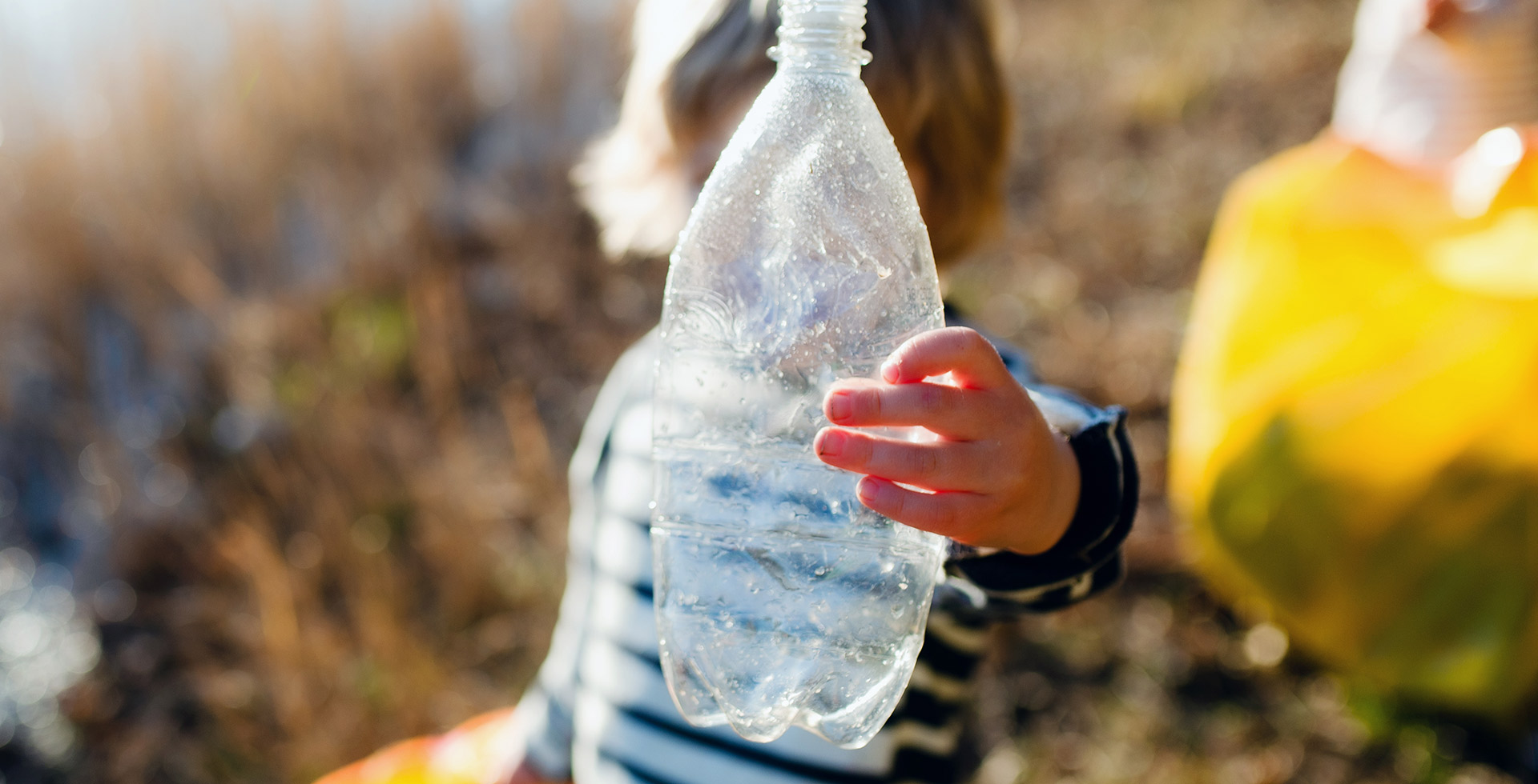 Child holding a plastic bottle against the sunlight - Unwrapping the potential of sustainable packaging