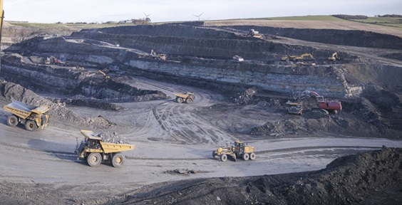 Picture of a worker in a coal mine with trucks in the background