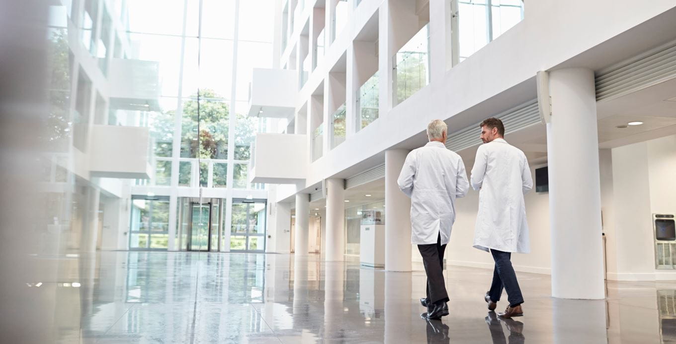 Image of a hospital building with two doctors walking and talking