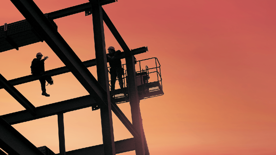 Silhouetted construction workers on a steel framework against an orange sunset sky.